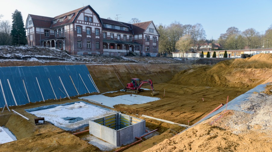 Baugrube, Rand zum Teil mit einer Plane abgedeckt Rechteck aus Schalbretter und Bagger in der Grube