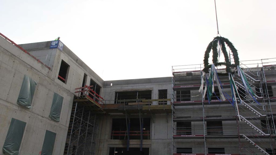 Der Richtkranz wird vom Kran hochgezogen im Hintergrund der Neubau.