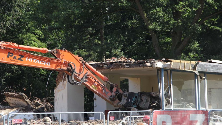 Ein Drittel des Erdgeschosses stehen noch. Ein Bagger greift mit seiner Schaufel hinein.