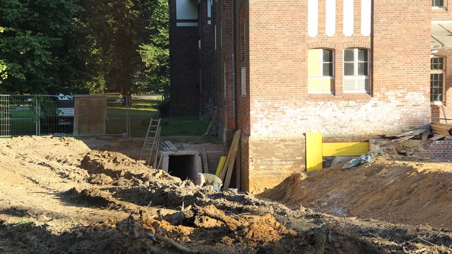 Geöffnete Baugrube mit einer Betonbodenplatte. Am Ende ist Hasus12 und der alte Medienkanal zu sehen.