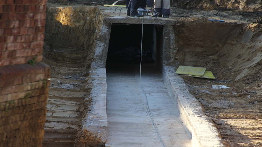 Geöffnete Baugrube mit einer Betonbodenplatte. Am Ende ist der alte Medienkanal zu sehen.