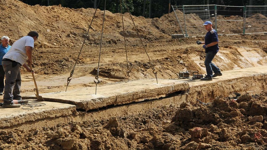 Öffnen des Medienkanals, herausheben der 1. Betonplatte durch einen Bagger.