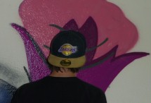 Sprayer mit Cap von hinten, betrachtet sein Werk eine Rose in Lila Pink